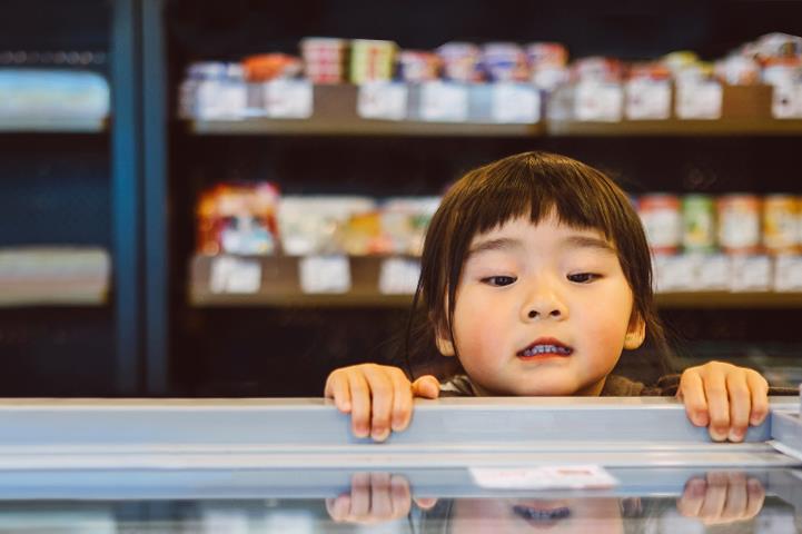 little girl peering over the edge and looking into a freezer chest at a supermarket