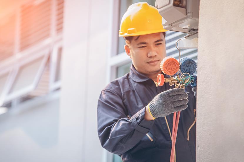 man wearing yellow hard hat and holding valve pump of air conditioning unit